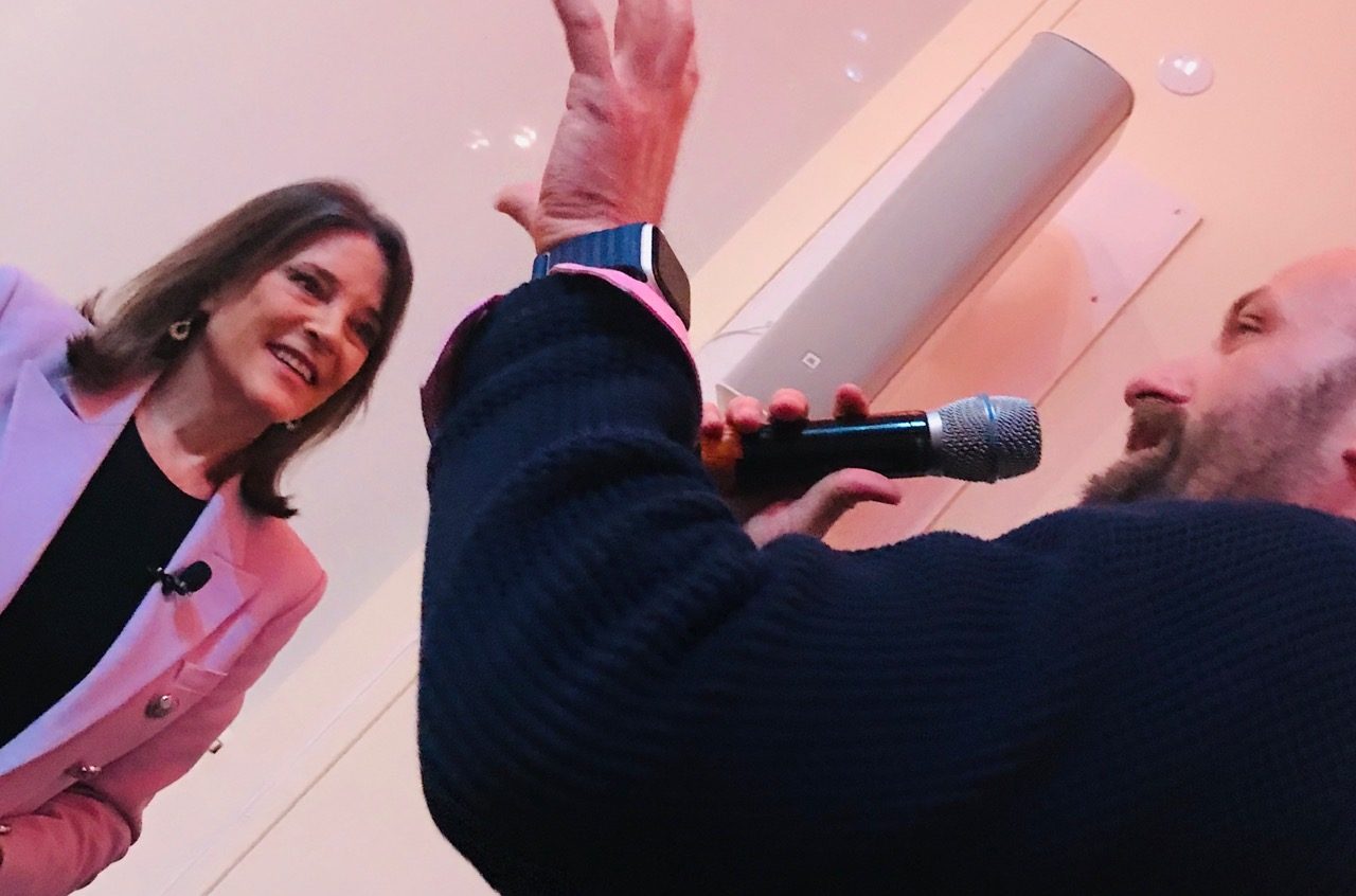 Russ on stage with a microphone beside Marianne Williamson