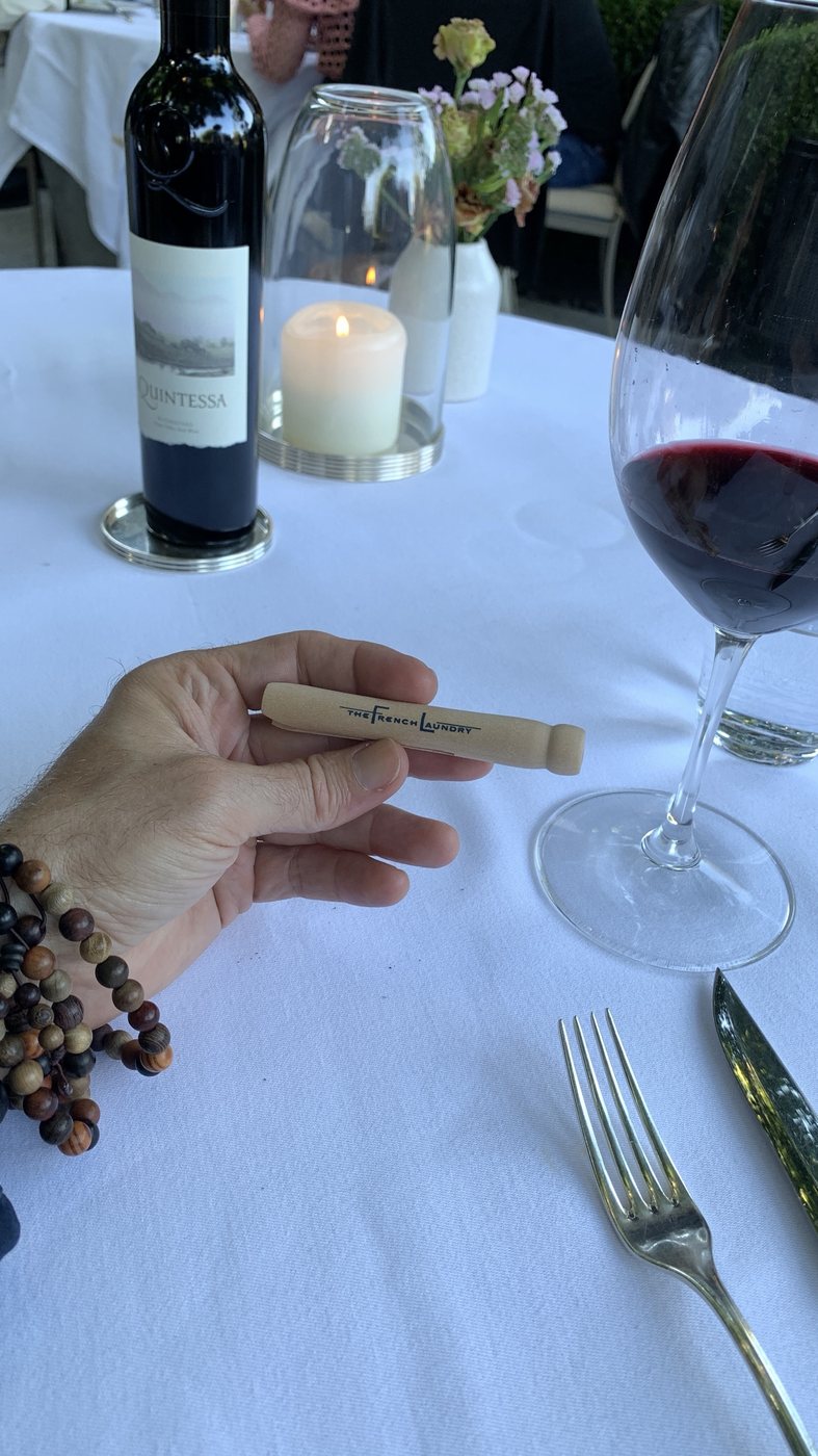 A clothespin from The French Laundry beside a glass of red wine and candlelight